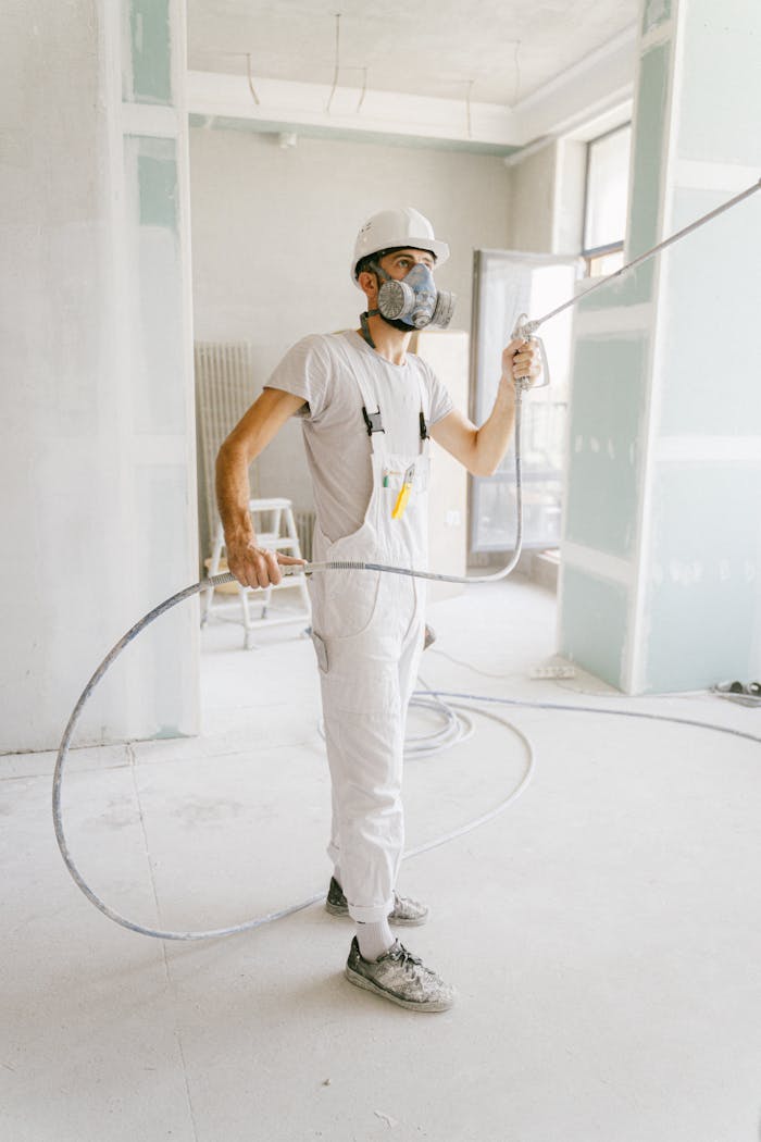 A construction worker in a white uniform using spray equipment inside a renovation site.